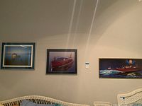 Wide shot of all three framed boat-themed prints on wall with wicker chair below