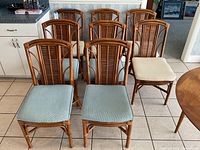 Set of eight rattan dining chairs arranged in two rows, showcasing four blue cushioned chairs in front and four white cushioned chairs behind.