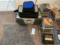 Sony boombox with a few accessories on top and CDs stacked next to it on carpeted floor near a wall.