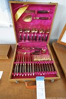 Full view of vintage flatware set inside wooden case with pink velvet-like lining and all utensils arranged and secured in place.