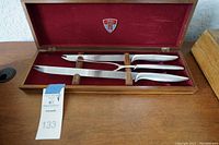 Closed walnut case open showing two carving knives and a meat fork secured inside with wooden holders and red velvet lining
