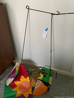 Yard flag frames standing on carpet next to colorful folded flags with sunflower and pumpkin designs.