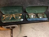 Two pairs of antique safety glasses each with original cases, shown on a surface.