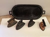 Four antique cast irons displayed with cast iron tray behind them, showing scale and shape differences.