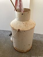 Full view of the white antique milk can, showing overall shape and surface wear with rust spots.
