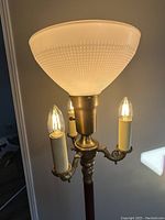 Close-up of the top section showing three lit candle-style lights and white textured glass shade