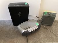 Full lot view showing black paper shredder, silver stereo unit, and beige Philips portable heater on a gray surface.