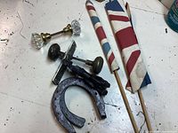 Photo showing three horseshoes, two vintage door knobs (one glass with brass fitting and one dark metal), and two small red, white, and blue fabric flags on wooden sticks.