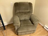 Front view of a greenish-brown La-Z-Boy recliner chair with cushioned armrests and padded backrest in a room with hardwood floor.