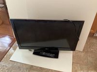 32 inch black LG television with a black remote control placed in front of it on a white board on a tiled floor.