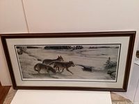 Framed print of three timber wolves in snowy landscape, titled 'Spring Thaw Timber Wolves' by Michael Dumas, shown full view leaning against wall.
