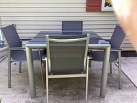 View of rectangular glass-top table with four sling chairs on concrete pad