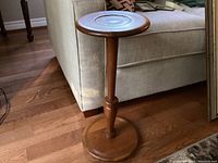 Full view of the wooden plant stand beside a couch showing round top and base with central column