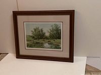 Framed watercolour art depicting cows grazing beside a pond with trees in the background