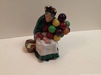 Photo of Royal Doulton Old Balloon Seller figurine showing the seated elderly woman with colorful balloons and basket.