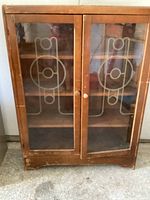Front view of antique wooden cabinet with two glass doors featuring etched geometric designs.