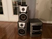 Sony stereo system including main unit and two speakers on hardwood floor near glass doors.