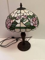 Full view of the Tiffany style lamp showing the stained glass floral shade with pink flowers and green leaves against a white glass background.