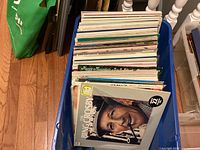 Blue plastic bin filled with approximately 25 vinyl record albums from the 1960s by various artists. Front album visible is a Bing Crosby album with his portrait on the cover.