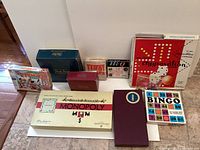 Overview photo showing an assortment of vintage board games and party games placed on a table. Games identified include Monopoly, Aggravation, Bingo, Memory, and others in various colored boxes.