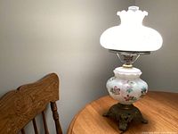 Vintage bedroom lamp with white floral glass and brass base on wooden table beside a carved wooden chair.