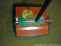 Top view of Bissell Super Gemini carpet sweeper on carpeted floor showing orange body, green detail, and chrome handle.