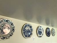 Group of five deep blue patterned dinner plates mounted on wall with metal hangers, various floral and scenic designs.