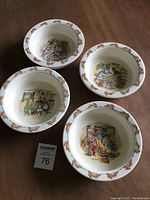 Four white bone china Bunnykins porridge bowls arranged together showing different illustrated scenes inside and bunny rim pattern