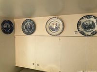 Four blue and white collectible plates mounted on wall above cabinets, showing size and display appearance.