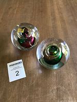 Two round studio crystal paperweights with colorful cores on a wooden surface, showing original Polish stickers on top.