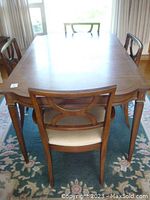 Photo showing entire dining table and four chairs around it, highlighting wood finish and chair design.