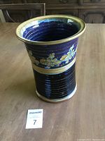 Full view of the vase showing its flared rim, ribbed blue midsection, and yellow floral motif band under the light beige rim.