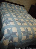 Blue and white patchwork quilt spread on bed showing repetitive star pattern and light blue borders.