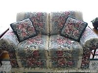 Front view of floral fabric two-seat sofa showing overall pattern and two matching decorative cushions.