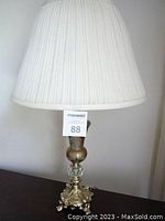 Full shot of the table lamp showing cream pleated lampshade and ornate gold footed base