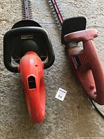 Two electric hedge trimmers side by side on concrete floor showing their overall length and shape.