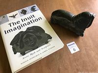 Stone carved walrus with 'The Inuit Imagination' book on wooden table, showing the size and the lot together.