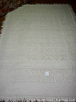 Full view of the rectangular cream wool rug on carpeted floor showing overall texture and tasselled edges.