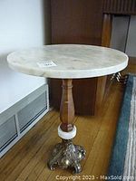 Front view of round white marble top and turned wood pedestal with ornate gold-tone base