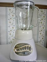 Front view of Oster blender showing control panel with 12 speed buttons and pulse option, glass pitcher on base.