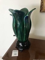 Full side view of the ceramic lamp showing green leaf-like petals and black base.