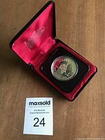 Silver dollar coin in open red satin-lined black display case with Royal Canadian Mint logo in lid.