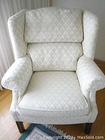 Front angle of off-white wingback armchair showing seat cushion and backrest upholstery with textile pattern.