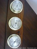 Front view of the vintage Taylor 3 gauge weather station showing thermometer, barometer, and hygrometer dials with brass-colored rims on a wooden plaque.