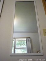 Full view of narrow tall rectangular mirror with white wood frame hung on wall
