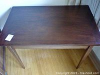 Top angled view of dark walnut wood rectangular end table showing smooth dark wood grain surface and four tapered legs on light wood floor under natural lighting.
