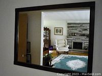 Mirror hanging on a wall reflecting a room with a fireplace and chair, showing the size and clarity of the mirror.