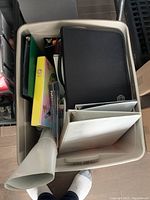 Top-down view into plastic bin showing variety of binders and folders inside.