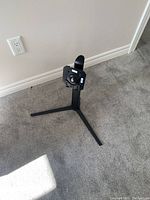 Photo of a black metal computer stand with a tripod base and adjustable mounting bracket placed on carpeted floor