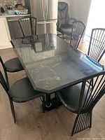 Photo of rectangular kitchen table with black marble-like top and six matching black metal frame chairs with padded black seats.